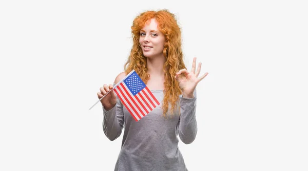 優秀なシンボルの指で サインをしている若い赤毛の女性はアメリカ合衆国の国旗を保持しています — ストック写真