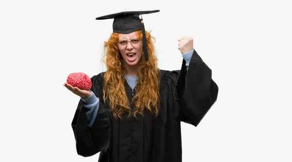 Jovem Estudante Ruiva Vestindo Uniforme Graduado Segurando Cérebro Irritado Frustrado — Fotografia de Stock