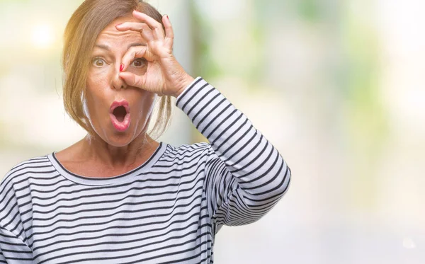 Orta yaş ok jest yapıyor izole arka plan üzerine İspanyol kadın kıdemli sürpriz yüz, göz parmaklarının arasından seyir ile şok. İmansız ifade.