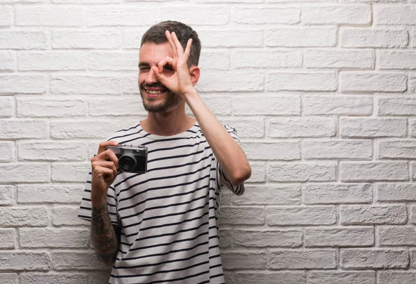 Mutlu yüz el parmaklarının arasından seyir göz üzerinde ok işaretiyle yapıyor gülümseyen ile beyaz tuğla duvarın üzerinden vintage fotoğraf makinesi ayakta tutan genç adam
