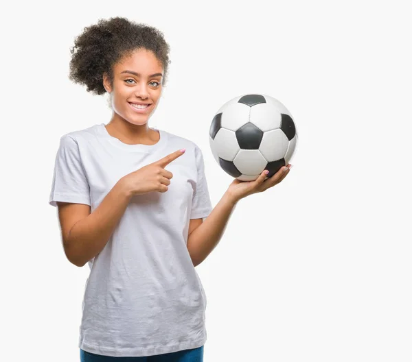 年轻美丽的美国黑人举行足球足球在孤立的背景很高兴指向用手和手指 — 图库照片