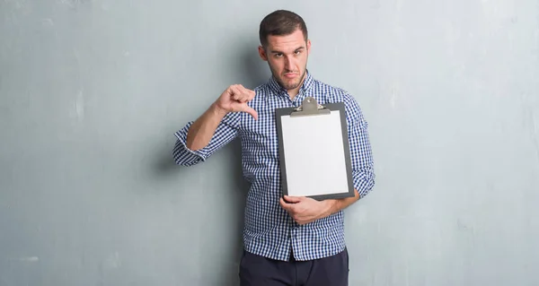 Young Caucasian Man Grey Grunge Wall Holding Clipboard Angry Face — Stock Photo, Image