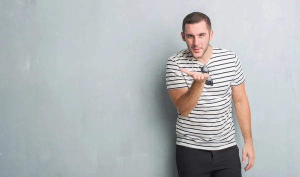 Joven Hombre Caucásico Sobre Gris Pared Grunge Mirando Cámara Soplando — Foto de Stock