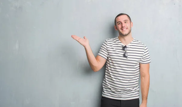 Young Caucasian Man Grey Grunge Wall Smiling Cheerful Presenting Pointing — Stock Photo, Image