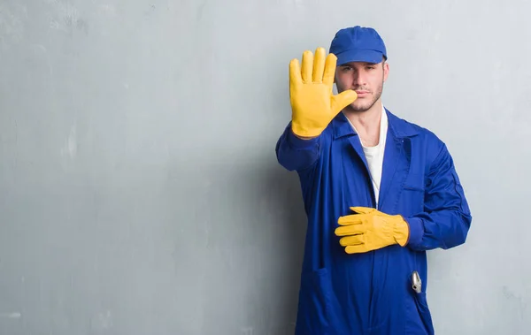 Joven Caucásico Hombre Sobre Gris Grunge Pared Usando Uniforme Mecánico — Foto de Stock