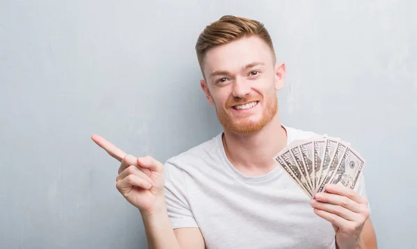 Young Redhead Man Grey Grunge Wall Holding Dollars Very Happy — Stock Photo, Image