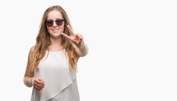 勝利のサインをやって指を表示するカメラを笑みを浮かべてサングラスをかけて若いブロンドの女性 — ストック写真