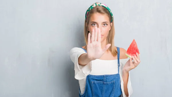 美丽的年轻妇女在垃圾灰色墙壁吃西瓜用张开手做停止标志以严肃和自信的表示 防御手势 — 图库照片