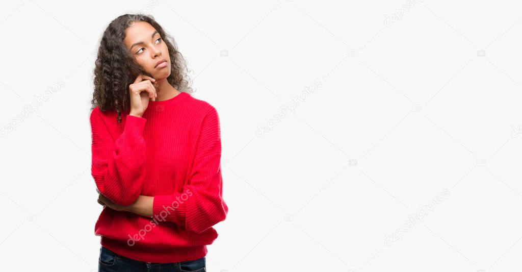Young hispanic woman wearing red sweater with hand on chin thinking about question, pensive expression. Smiling with thoughtful face. Doubt concept.