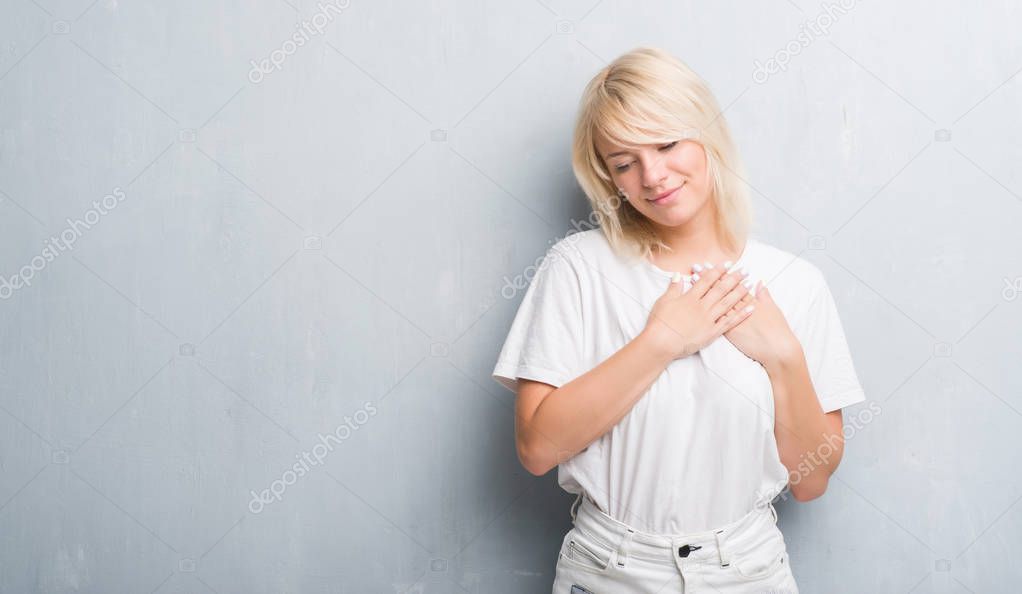 Adult caucasian woman over grunge grey wall smiling with hands on chest with closed eyes and grateful gesture on face. Health concept.