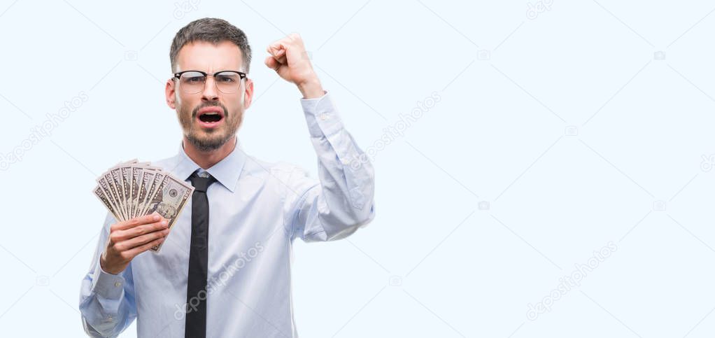Young hipster business man holding dollars annoyed and frustrated shouting with anger, crazy and yelling with raised hand, anger concept