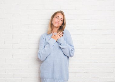 Üzerinde beyaz tuğla duvar ile gülümseyen güzel genç kadın kapalı gözler ve yüzünde minnettar jest ile göğüs üzerinde eller. Sağlık kavramı.