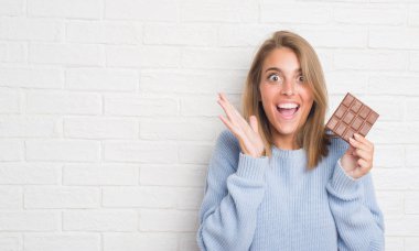 Beyaz tuğla duvar yeme üzerinde güzel genç kadın büyük gülümseme ile çığlık zaferini kutluyor ve ellerini kaldırdı çok mutlu ve heyecanlı, kazanan ifade çikolata