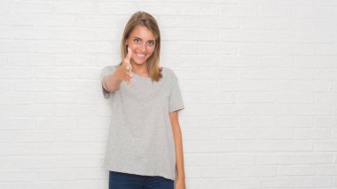 Beyaz tuğla duvar dostu sunan el sıkışma tebrik ve davet edici olarak gülümseyen güzel genç kadın. Başarılı iş.