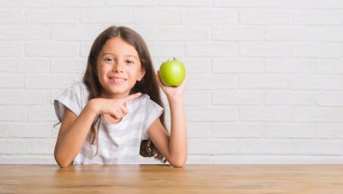 Taze yeşil elma el ve parmak ile işaret çok mutlu yemek masada oturan genç İspanyol çocuk