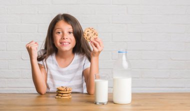 Duygu tezahürat süt içme ve gurur çığlık ve zafer ve başarı çok heyecanlı, kutluyor çikolata bisküvi yemek masada oturan genç İspanyol çocuk
