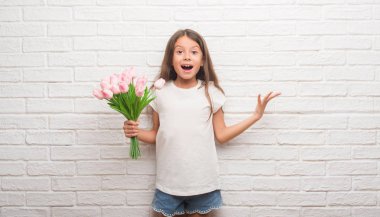 Beyaz tuğla duvar çiçek anneler günü üzerinde çok mutlu ve heyecanlı, kocaman bir gülümseme ile çığlık ve ellerini kaldırdı kazanan ifade kutluyor zafer tutan genç İspanyol çocuk