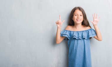 Gösterilen ve parmakları ile işaret grunge gri duvarın üzerinden genç İspanyol çocuğun kendinden emin ve mutlu gülümseyerek süre yedi numara.