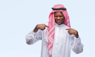 Yüzünde gülümseme ile kendinden emin görünüyorsun, kendini gururlu ve mutlu parmakları ile işaret izole arka plan üzerinde geleneksel keffiyeh giyen genç Arapça Afrika adam.