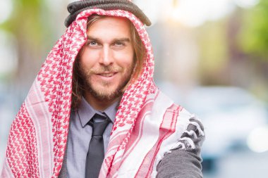 Genç yakışıklı Arap adam uzun saçlı olarak tebrik ve konuksever dost sunan karşılıklı gülümseyen izole arka plan üzerinde keffiyeh giyiyor. Başarılı iş.