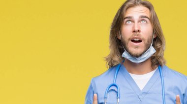 İzole arka plan üzerinde uzun saçlı Genç yakışıklı Doktor adam hayret ve yukarıya bakıp parmakları ile işaret şaşırttı ve silah kaldırdı.