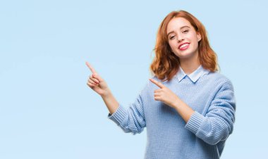 İzole arka plan gülümseyen ve iki elleri ve parmakları ile tarafına işaret kamera bakarak kış kazak giyen genç güzel kadın.