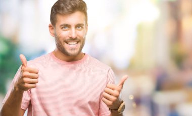 Yakışıklı delikanlı izole arka plan başarı işareti el ile pozitif jest yapıyor üzerinde başparmak gülümseyen ve mutlu. Neşeli bir ifadeyle, kazanan jest kameraya bakıyor.