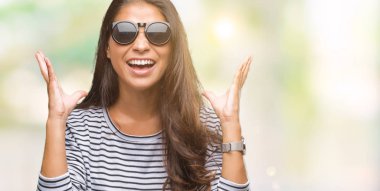 Genç güzel Arap kadın deli ve çığlık kaldırdı ve kapalı gözleri heyecanlı silah ile başarı için deli kutluyor izole arka plan üzerinde güneş gözlüğü takıyor. Kazanan kavramı