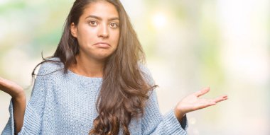 İzole arka plan clueless ve şaşkın bir ifadeyle kollar ve eller kaldırdı üzerinde kış kazak giyen genç güzel Arap kadın. Şüphe kavramı.