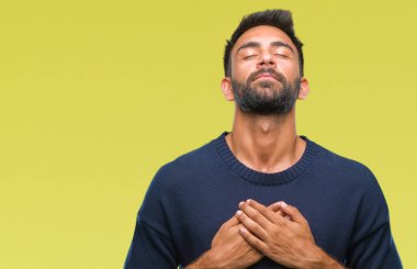 Göğüs kapalı gözler ve yüzünde minnettar jest ile yetişkin İspanyol adam ile gülümseyen izole arka plan üzerinde eller. Sağlık kavramı.