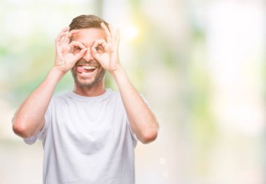 Yakışıklı delikanlı, dilini parmaklarının arasından baktığını yapışmasını dürbün gibi ok jest yapıyor izole arka plan üzerinde. Deli ifade.