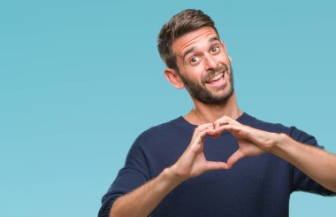 Genç yakışıklı adam aşık kalp simgesi ve elleriyle şekil gösteren gülümseyen izole arka plan üzerinde kış kazak giyiyor. Romantik kavramı.