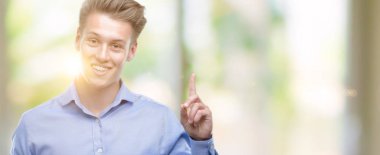 Genç yakışıklı sarışın adam Smartphone sürpriz bir fikir ya da soru işaret parmağı gülen yüz, bir numara ile kullanma