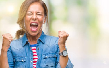 Gülümseyen ve başarı için çığlık orta yaş üst düzey İspanyol kadın izole arka plan çok mutlu ve heyecanlı kaldırdı, silah ile kazanan jest yapıyor. Kutlama kavramı.