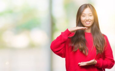 Üzerinde kış kazak giyen genç Asyalı kadın arka plan ile büyük ve büyük boy işaret, ölçü birimi sembol gösteren el eller izole. Kameraya bakarak gülümsüyordu. Ölçüm kavramı.