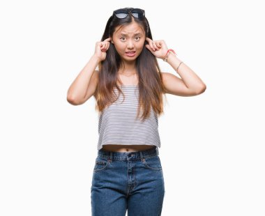 Genç Asyalı kadın parmakları ile yüksek sesle müzik gürültü rahatsız ifade kulaklarıyla kapsayan izole arka plan üzerinde güneş gözlüğü takıyor. Sağır kavramı.