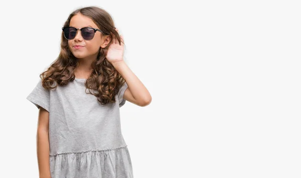 黑发西班牙裔女孩戴着墨镜微笑着用手在耳边听着谣言或流言蜚语 耳聋概念 — 图库照片