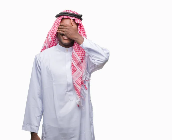 若いアラビアのアフリカの男は微笑し 笑う顔驚きの目を覆っている手で孤立した背景に伝統的なクーフィーヤを着てします 視覚障害者の概念 — ストック写真