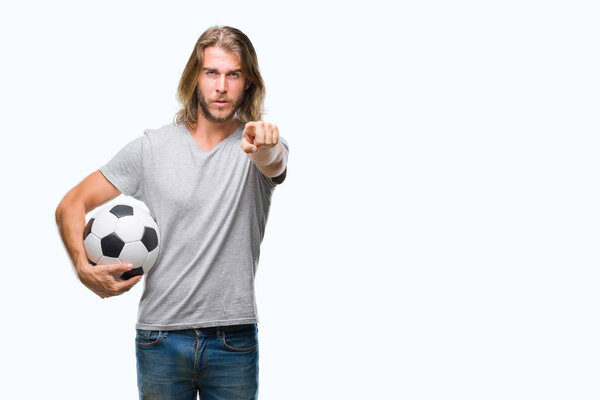 Young handsome man with long hair over isolated background holding football ball pointing with finger to the camera and to you, hand sign, positive and confident gesture from the front