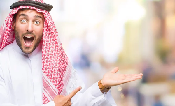 Keffiyeh hayret ve el ile sunulması ve parmak ile işaret ederken kameraya gülümseyen izole arka plan üzerinde giyen genç yakışıklı adam.