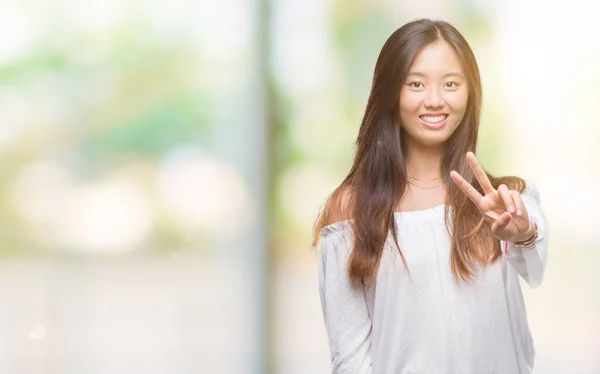 年轻的亚洲妇女在孤立的背景下微笑着看着相机 显示手指做胜利的标志 第二个 — 图库照片