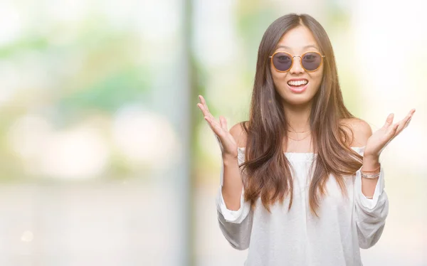 年轻的亚洲妇女戴着太阳镜在孤立的背景下庆祝疯狂和惊讶的成功与手臂举起 睁开眼睛尖叫兴奋 赢家理念 — 图库照片