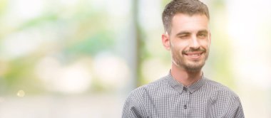 Genç hipster adam seksi bir ifadeyle, neşeli ve mutlu yüzünü kameraya bakarak göz kırpıyor.