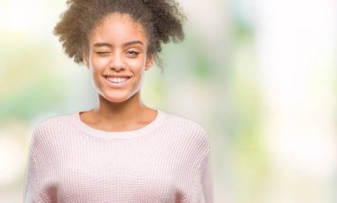 Seksi bir ifadeyle, neşeli ve mutlu yüzünü kameraya bakarak göz kırpıyor izole arka plan üzerinde kış kazak giyen genç afro Amerikan kadın.