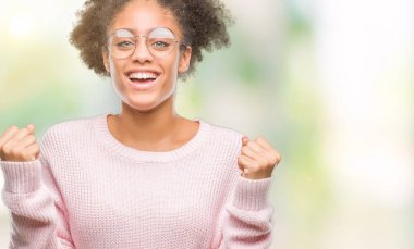 İzole arka plan üzerinde kutluyor gözlük takan genç afro Amerikalı kadın şaşırttı ve silah ile başarı için yükseltilmiş ve açık gözler hayrete düşürdü. Kazanan kavramı.