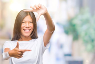 Genç Asyalı kadın elle yapma çerçeve ve parmakları ile mutlu yüz gülümseyen izole arka plan üzerinde. Yaratıcılık ve Fotoğrafçılık kavramı.