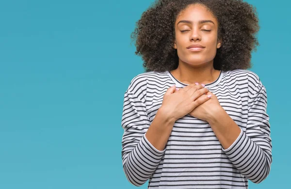 Young afro american woman over isolated background smiling with hands on chest with closed eyes and grateful gesture on face. Health concept.