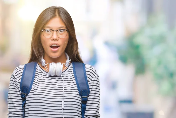 若いアジア学生の女性の身に着けているヘッドフォンと恐れ 驚きの表情でショックを受けて孤立の背景にバックパックの恐怖顔を興奮 — ストック写真
