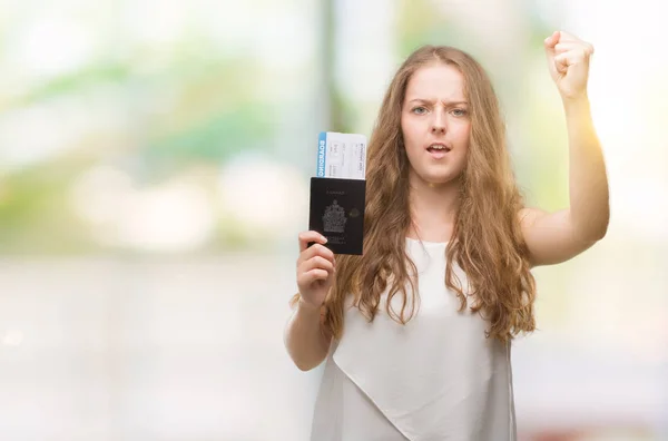 Young blonde woman holding passport of canada and boarding pass annoyed and frustrated shouting with anger, crazy and yelling with raised hand, anger concept