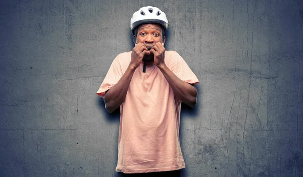 Black man wearing bike helmet terrified and nervous expressing anxiety and panic gesture, overwhelmed